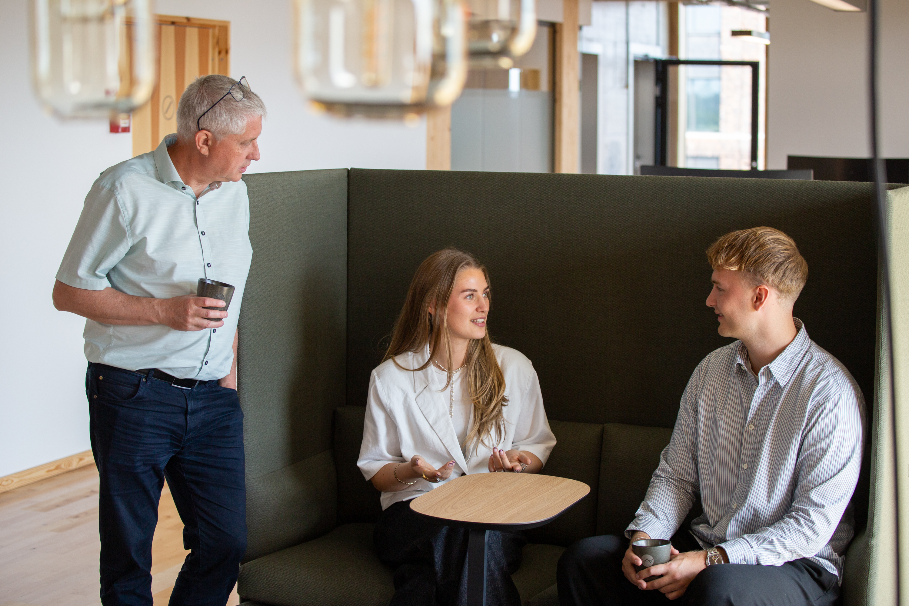 Tre kollegaer deler leasing erfaringer i kontorets lounge område.