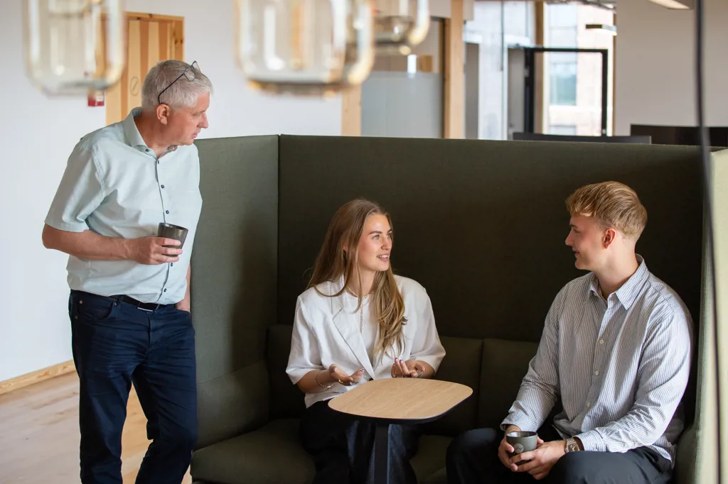 Tre kollegaer deler leasing erfaringer i kontorets lounge område.