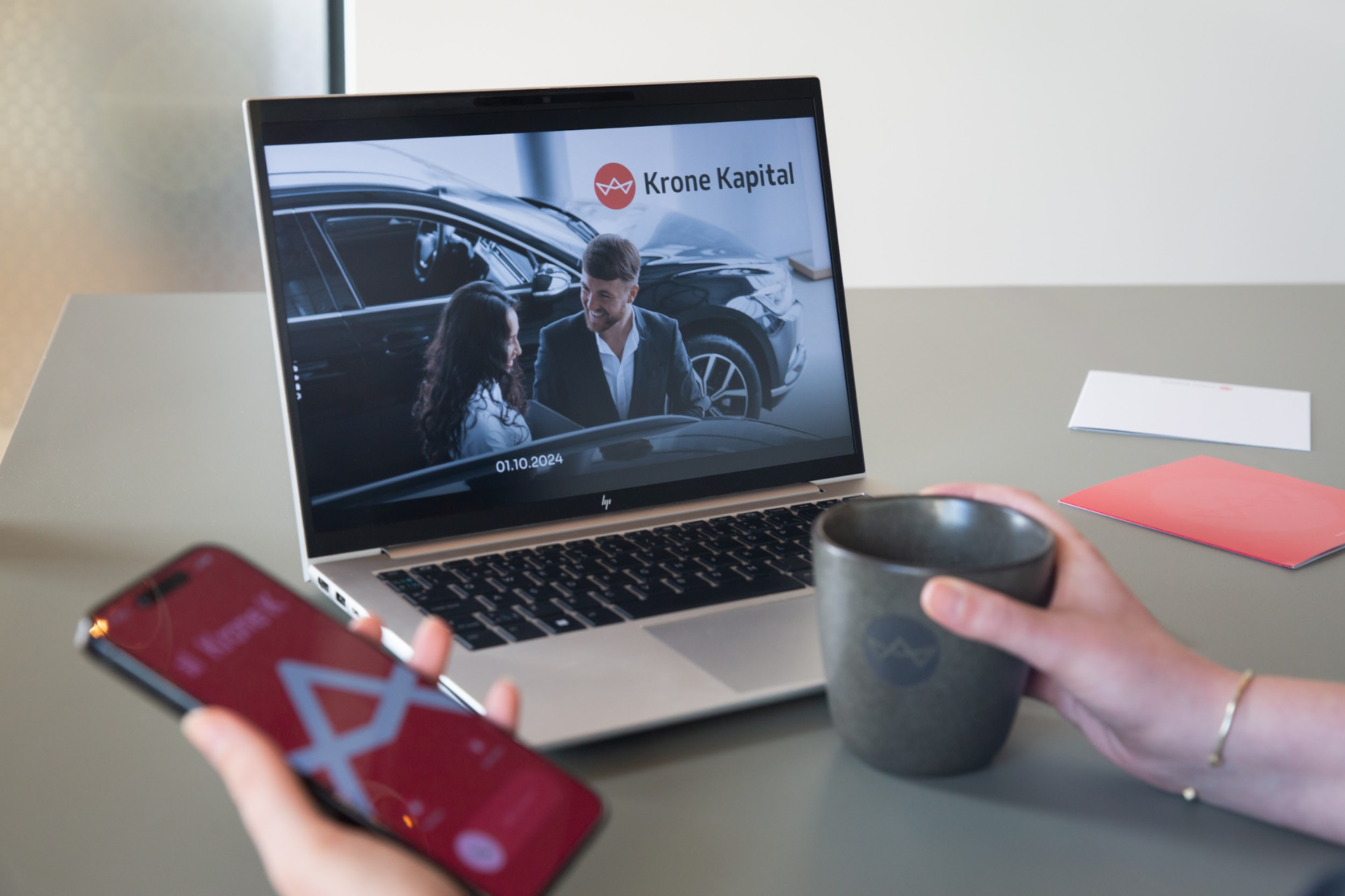 Kollega holder en kaffekop med Krone Kapital logo samt en telefon med et opkald fra Krone Kapital. Uden vandmærke.