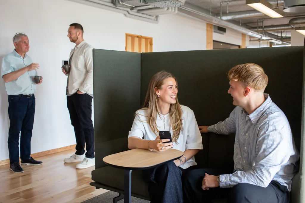 Uformel stemning på kontoret. Nogle sidder i sofaen og taler andre står bagved med kaffe i hånden.